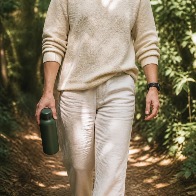 A person wearing a fitness tracker while walking outdoors with a water bottle